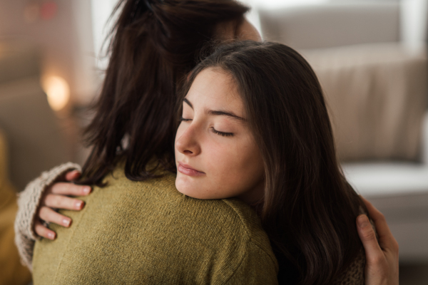 Young teenage girl hugging her mother at home.