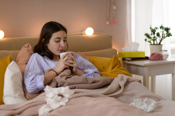 Sick teenage girl laying in bed with a cup of tea.