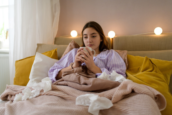 Sick teenage girl laying in bed with a cup of tea.