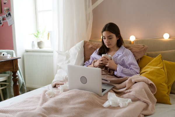 Sick teenage girl laying in the bed with a laptop.