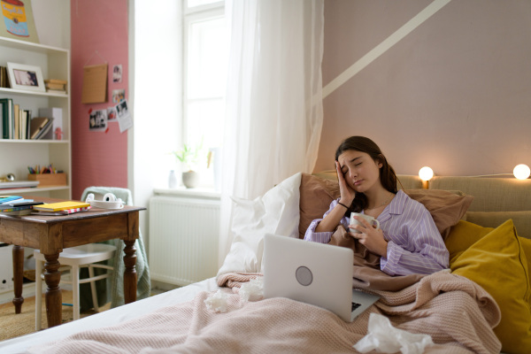 Sick teenage girl laying in the bed with a laptop.