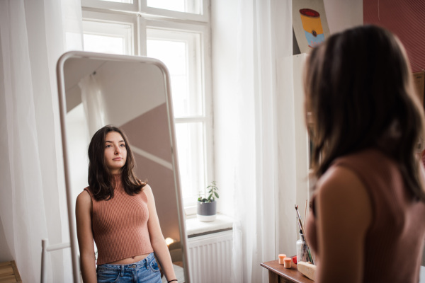 Young teenage girl looking in the mirror in the room.