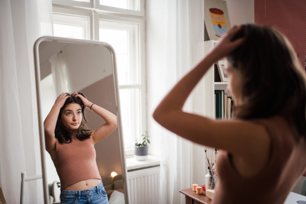 Young teenage girl looking in the mirror in the room.