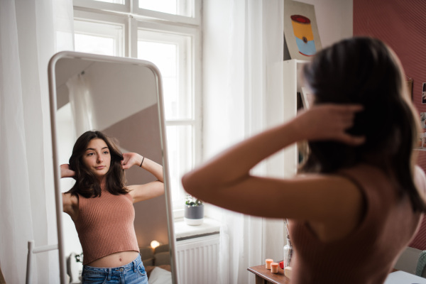 Young teenage girl looking in the mirror in the room.