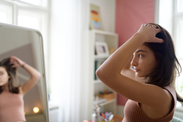 Young teenage girl looking in the mirror in the room.