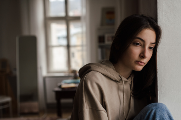 Unhappy teenage girl sitting in home and looking out of the window.