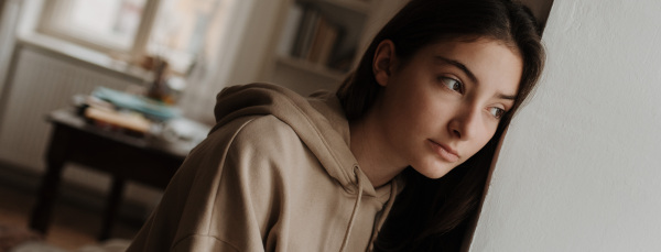 Unhappy teenage girl sitting in home and looking out of the window.