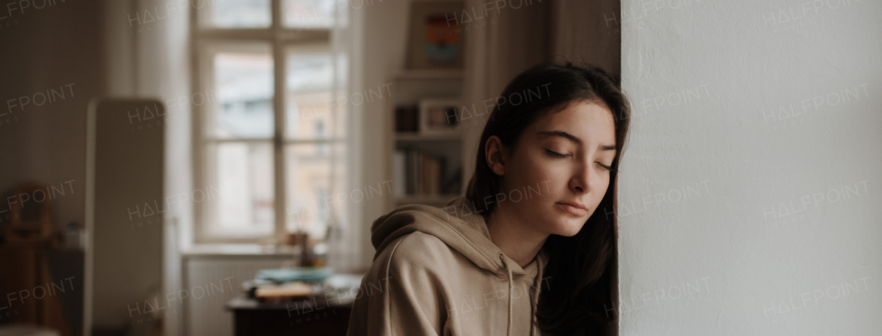 Unhappy teenage girl sitting in home and looking out of the window.