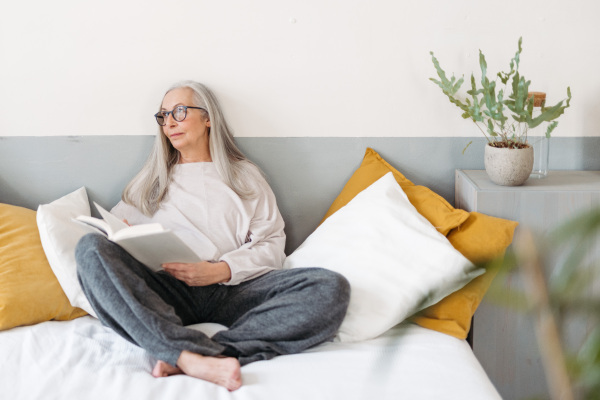 Senior woman reading a book in her bed, enjoying time alone i her apartment.