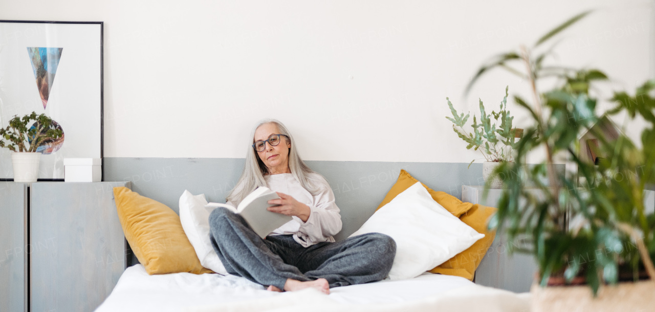 Senior woman reading a book in her bed, enjoying time alone i her apartment.