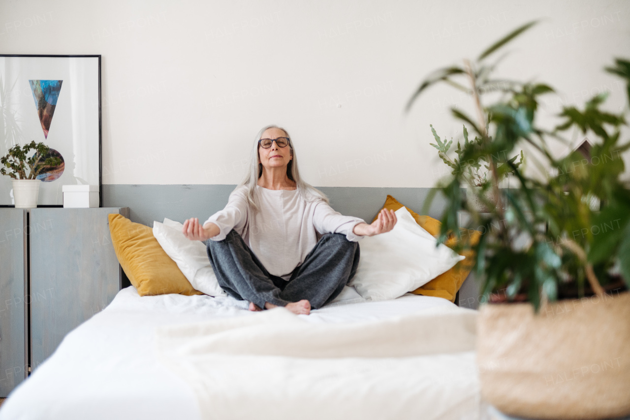 Senior woman doing yoga and meditating on a bed.