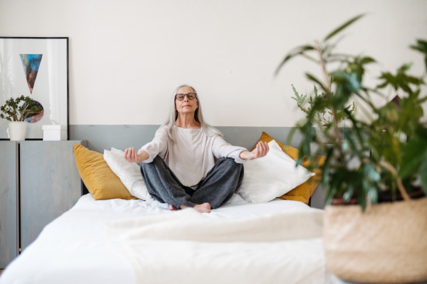 Senior woman doing yoga and meditating on a bed.