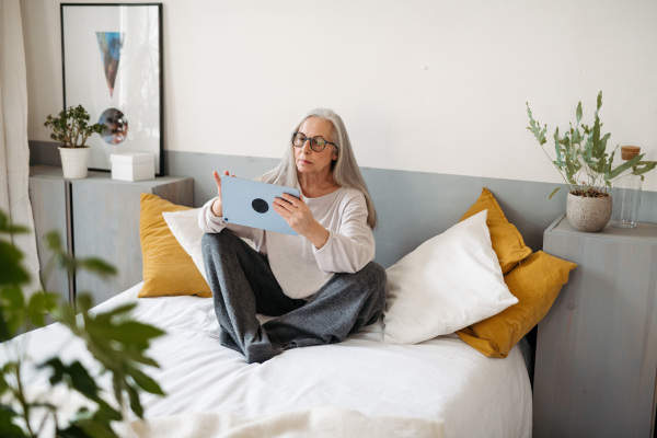 Senior woman sitting on a bed with a digital tablet.