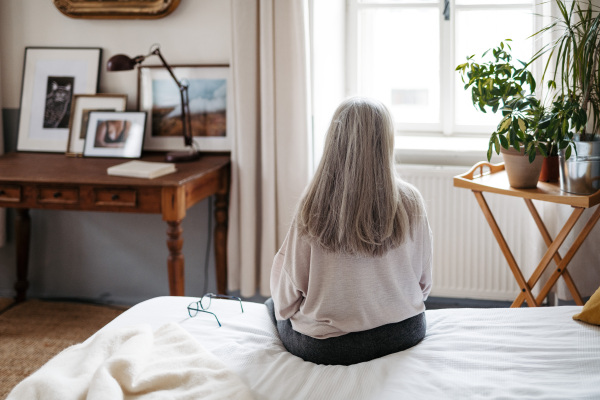 Rear view of senior woman sitting on her bed.