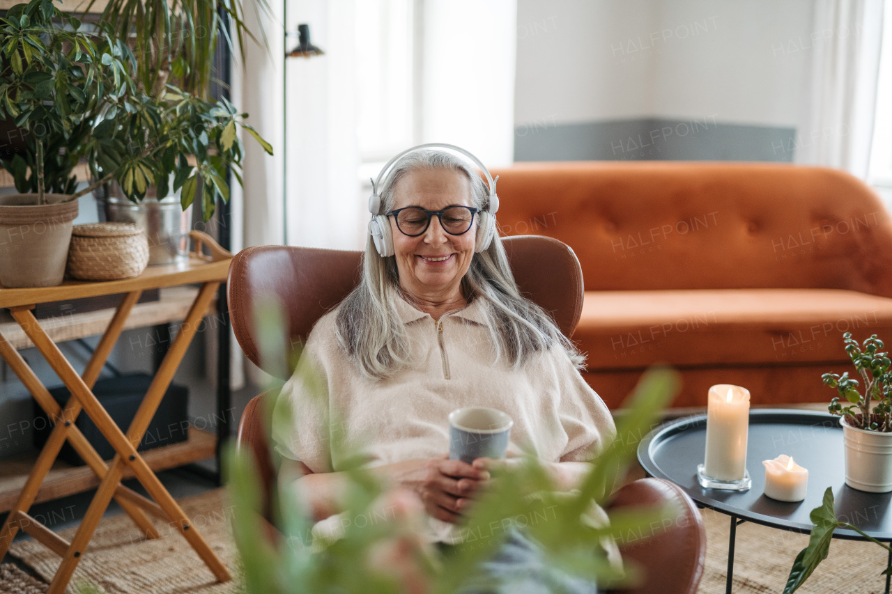 Senior woman resting with cup of tea in a living room, listening music.