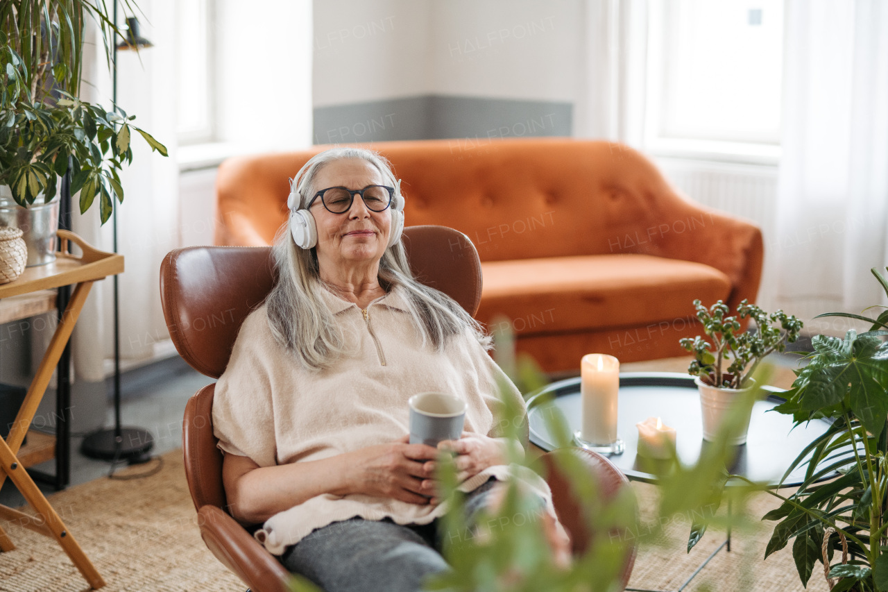 Senior woman resting with cup of tea in a living room, listening music.