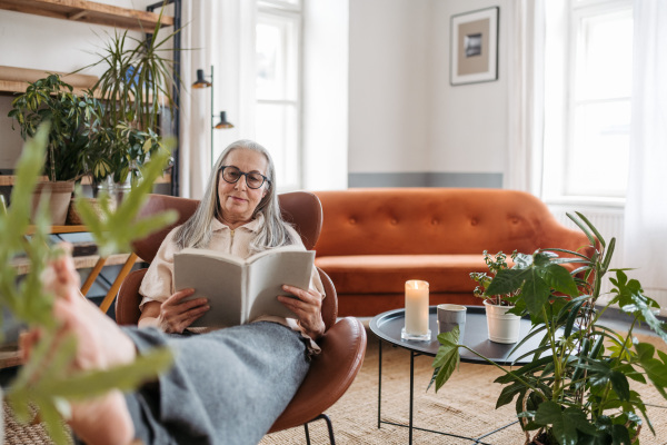 Senior woman reading a book, enjoying time alone in her apartment.