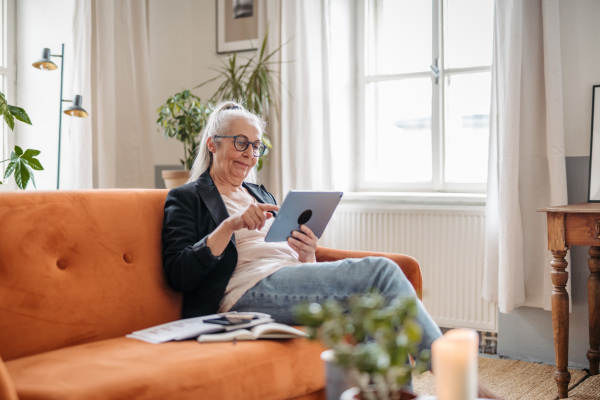 Senior woman resting on a sofa with a digital tablet.