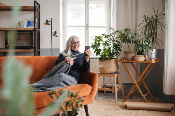 Senior woman resting on a sofa with a smartphone.