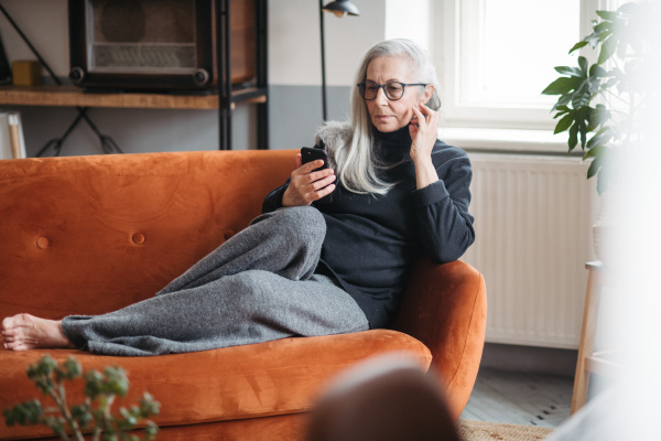 Senior woman resting on a sofa with a smartphone.