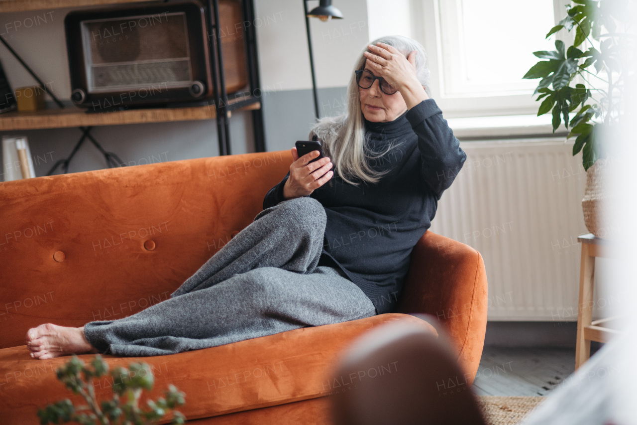 Senior woman resting on a sofa with a smartphone.