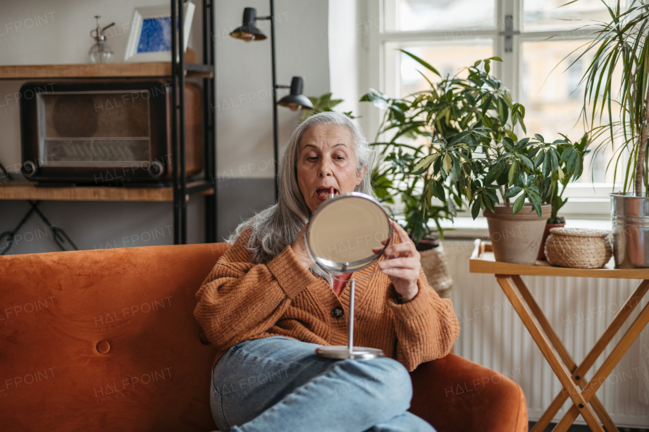 Senior woman doing her make-up, sitting in living room.