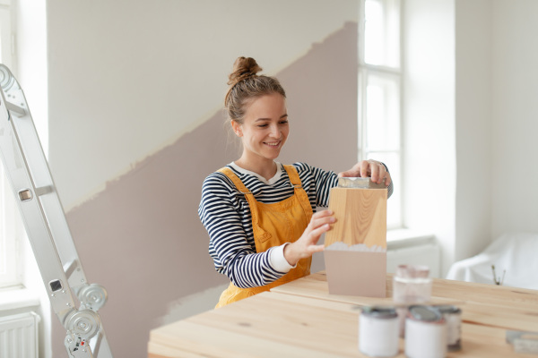 Happy young woman remaking shelf in her house. Concept of reusing materials and sustainable lifestyle.