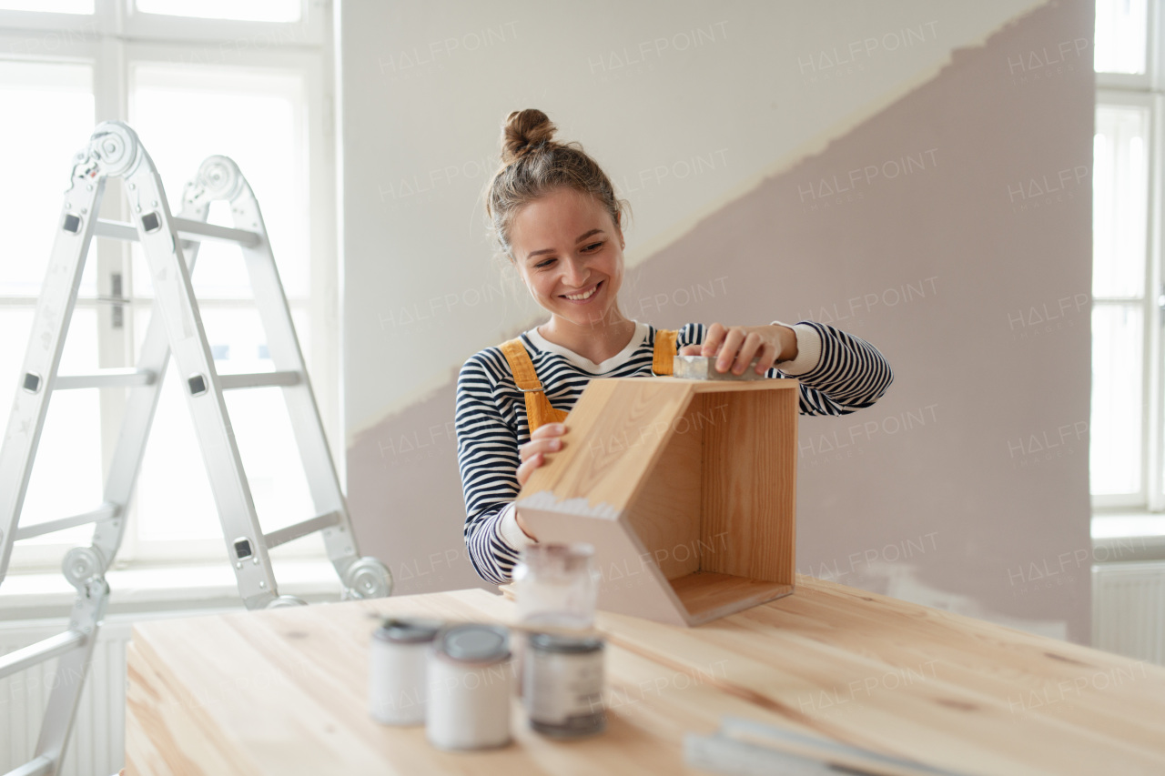 Portrait of young woman remaking shelf in her house. Concept of reusing materials and sustainable lifestyle.