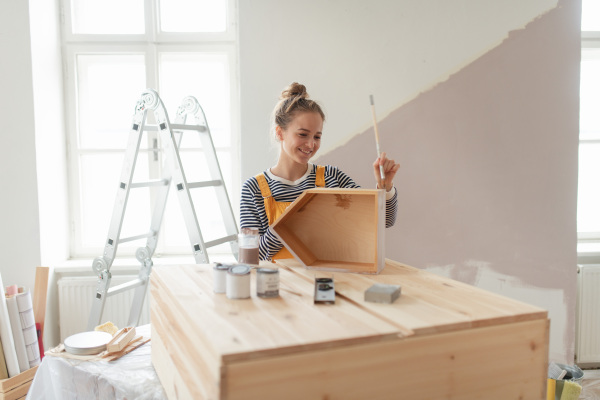 Happy young woman remaking shelf in her house. Concept of reusing materials and sustainable lifestyle.