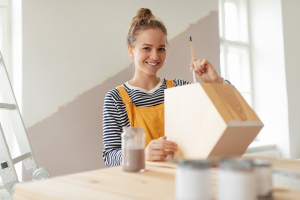 Happy young woman remaking shelf in her house. Concept of reusing materials and sustainable lifestyle.