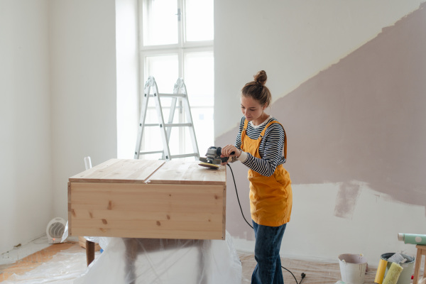 Happy young woman remaking wooden cabinet in her house. Concept of reusing materials and sustainable lifestyle.