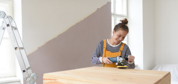 Happy young woman remaking wooden cabinet in her house. Concept of reusing materials and sustainable lifestyle.