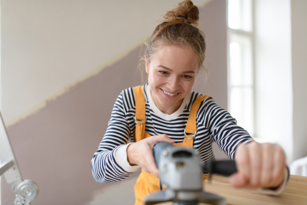 Happy young woman remaking wooden cabinet in her house. Concept of reusing materials and sustainable lifestyle.