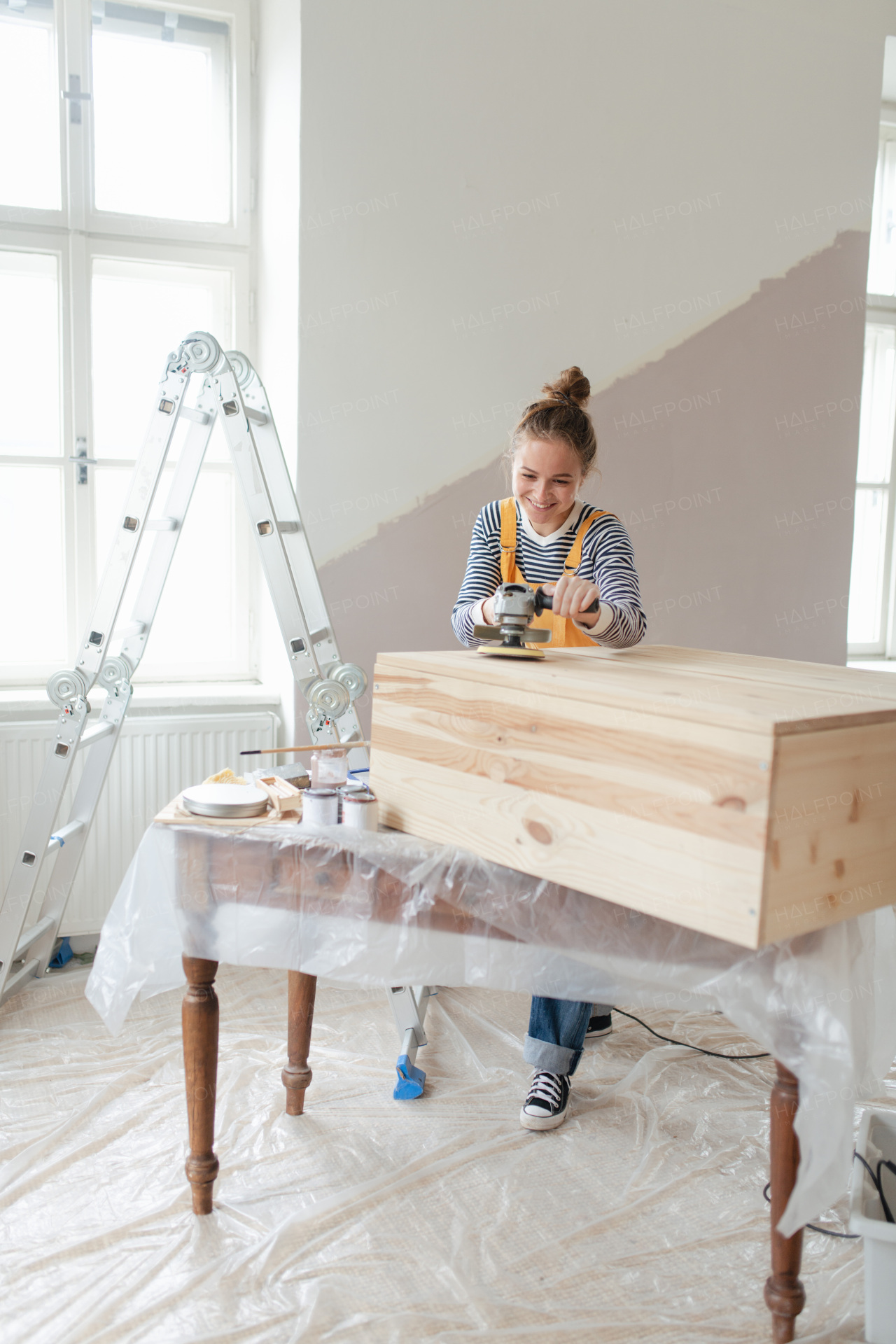 Happy young woman remaking wooden cabinet in her house. Concept of reusing materials and sustainable lifestyle.