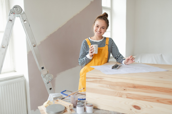 Happy young woman remaking wooden cabinet in her house. Concept of reusing materials and sustainable lifestyle.