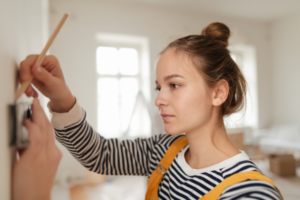 Young woman remaking her apartment, measuring wall with spirit level and hanging a shelf.