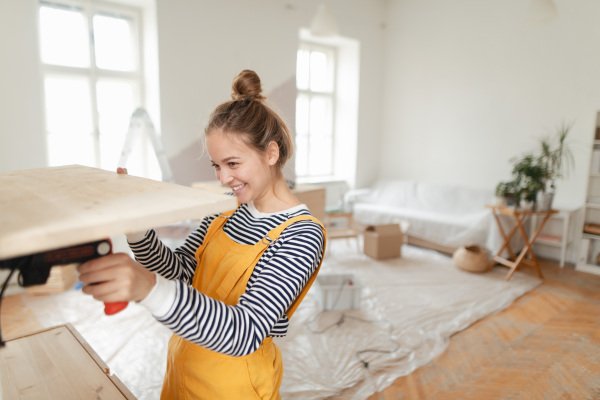 Happy young woman installing wooden shelf in her house. Concept of reusing materials and sustainable lifestyle.