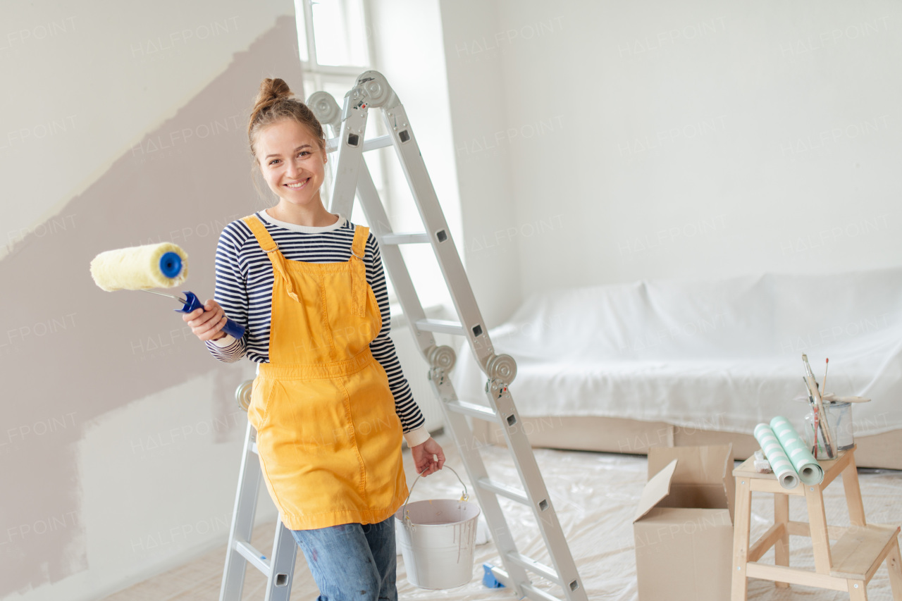 Happy young woman remaking her new house, painting walls. Concept of renovation, indepent women and sustainable lifestyle.