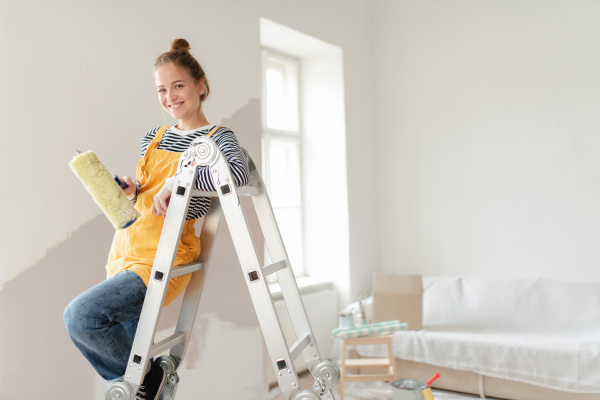 Happy young woman remaking her new house, painting walls. Concept of renovation, indepent women and sustainable lifestyle.