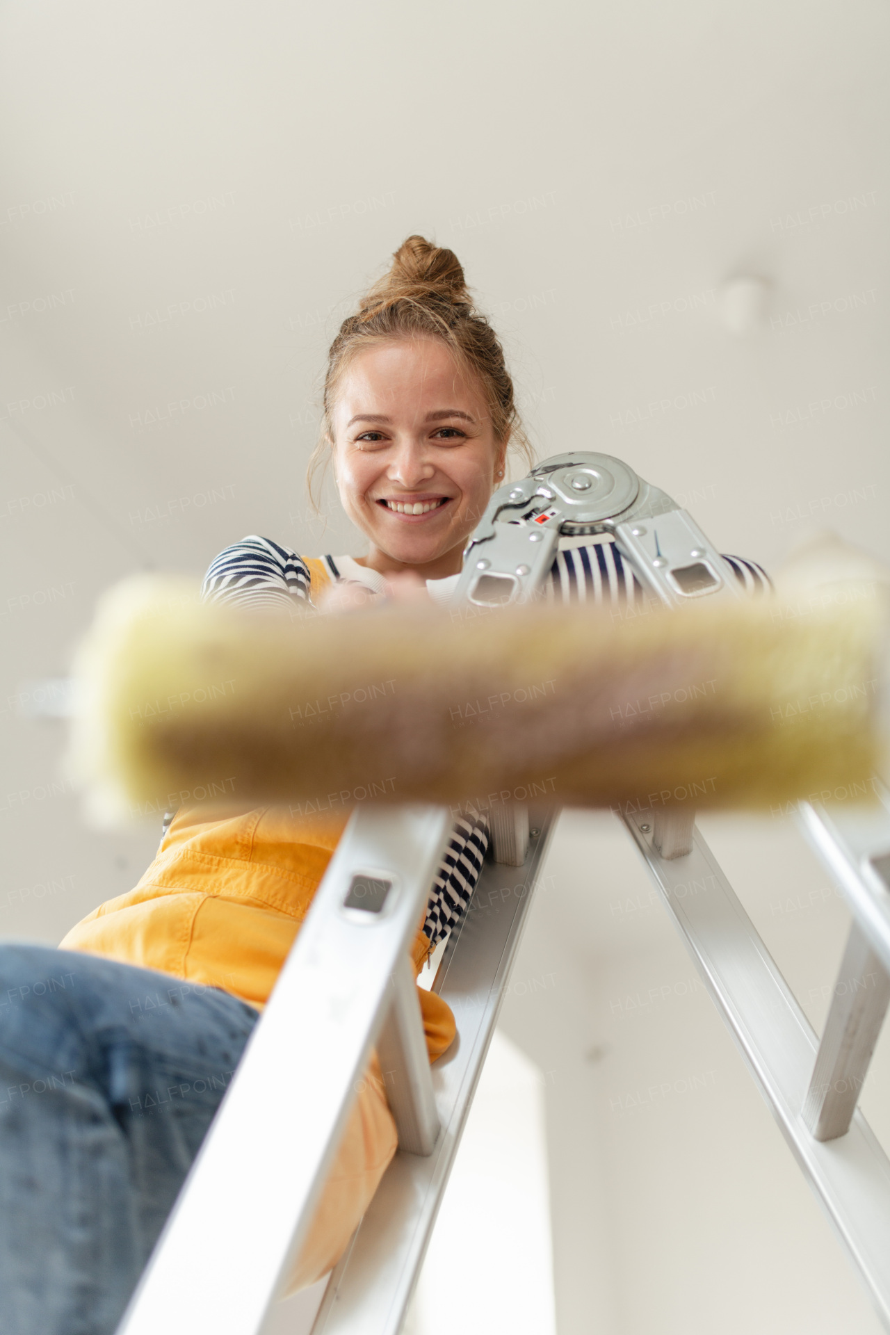 Low angle view of happy young woman remaking her new house, painting walls. Concept of renovation, indepent women and sustainable lifestyle.