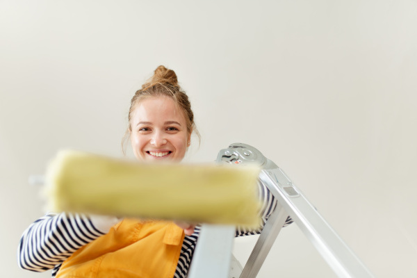 Happy young woman remaking her new house, painting walls. Concept of renovation, indepent women and sustainable lifestyle.