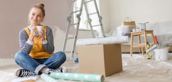 Happy young woman having break during renovation her house. Thinking about new projects. Concept of reusing materials and sustainable lifestyle.