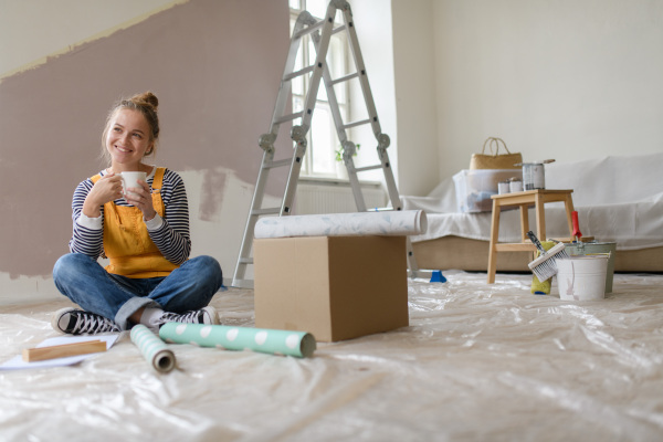 Happy young woman having break during renovation her house. Thinking about new projects. Concept of reusing materials and sustainable lifestyle.