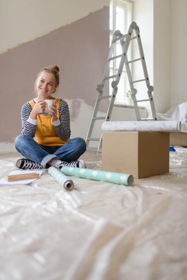 Happy young woman having break during renovation her house. Thinking about new projects. Concept of reusing materials and sustainable lifestyle.