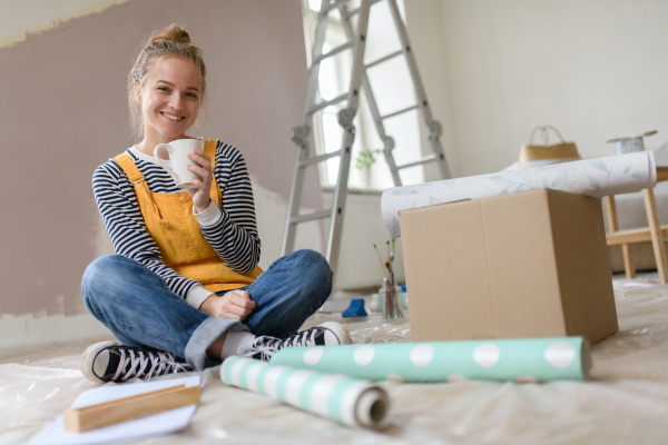 Happy young woman having break during renovation her house. Thinking about new projects. Concept of reusing materials and sustainable lifestyle.