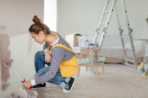 Happy young woman remaking her new house, painting walls. Concept of renovation, indepent women and sustainable lifestyle.