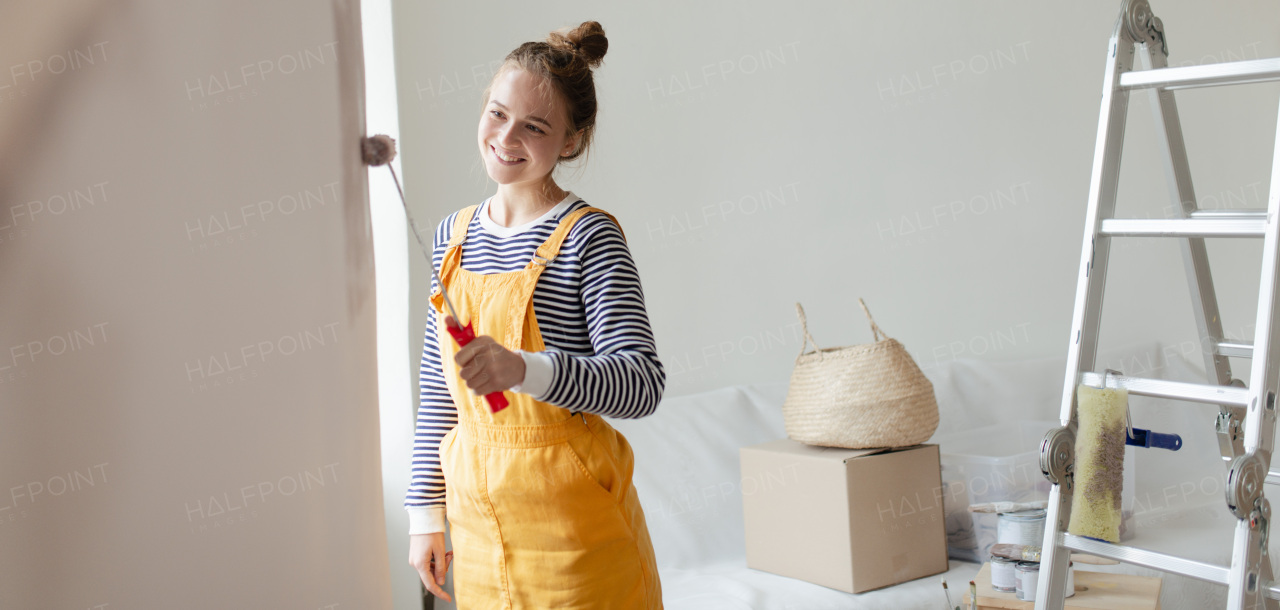 Happy young woman remaking her new house, painting walls. Concept of renovation, indepent women and sustainable lifestyle.