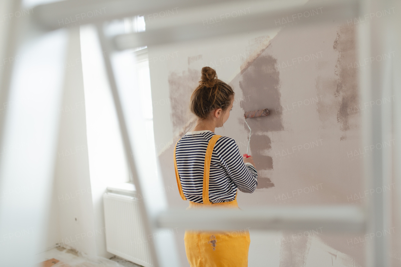 Happy young woman remaking her new house, painting walls. Concept of renovation, indepent women and sustainable lifestyle.