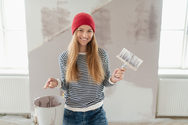 Happy young woman remaking her new house, painting walls. Concept of renovation, indepent women and sustainable lifestyle.