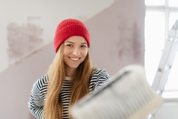 Portrait of happy young woman remaking her new house, painting walls. Concept of renovation, indepent women and sustainable lifestyle.